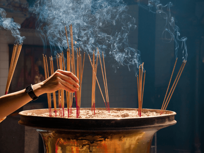 An image of a woman lighting incense sticks during a traditional Chinese funeral ritual, symbolising respect and remembrance for the deceased.
