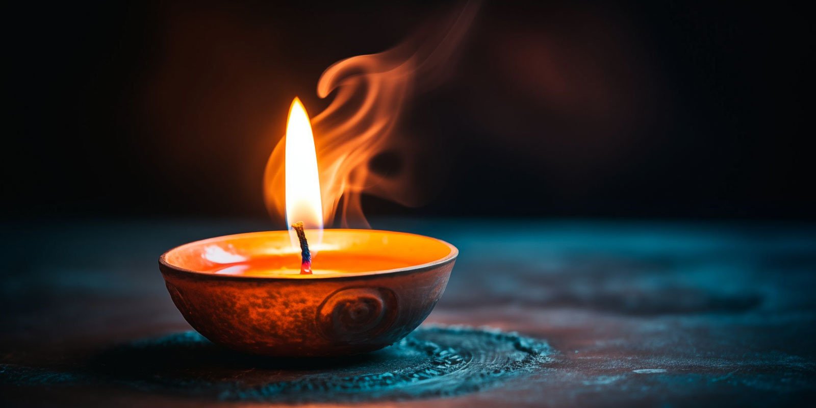 A single candle flame flickers in a small, intricately designed ceramic holder against a dark background. Soft light creates a warm, serene ambiance.