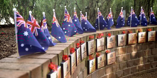 Australian flags and red poppies adorn a curved memorial wall with plaques at Macquarie Park Cemtery's Anzac Memorial