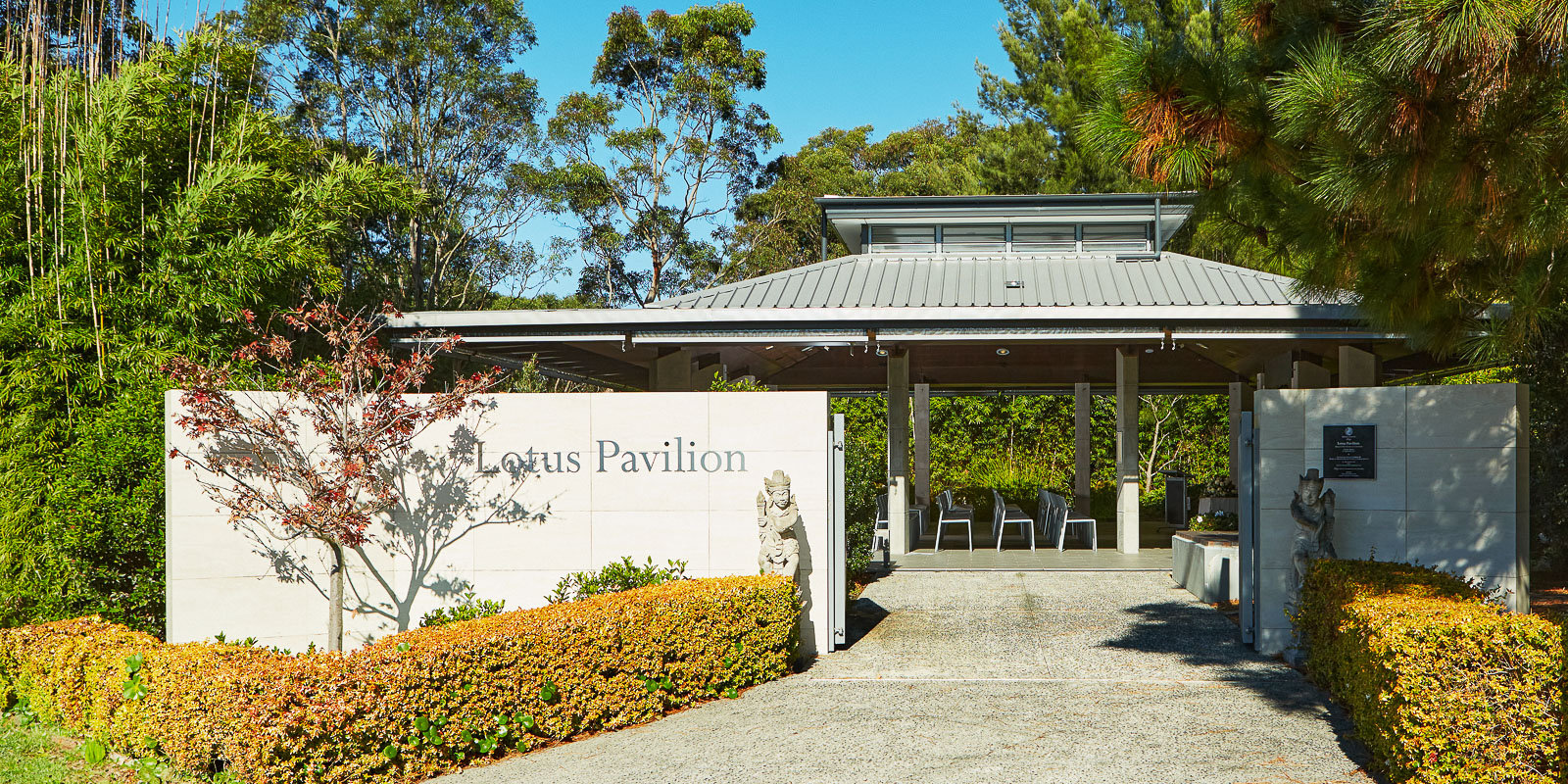 Entrance to the Lotus Pavilion, surrounded by greenery and landscaped hedges, with an open pavilion structure visible beyond the entry sign.