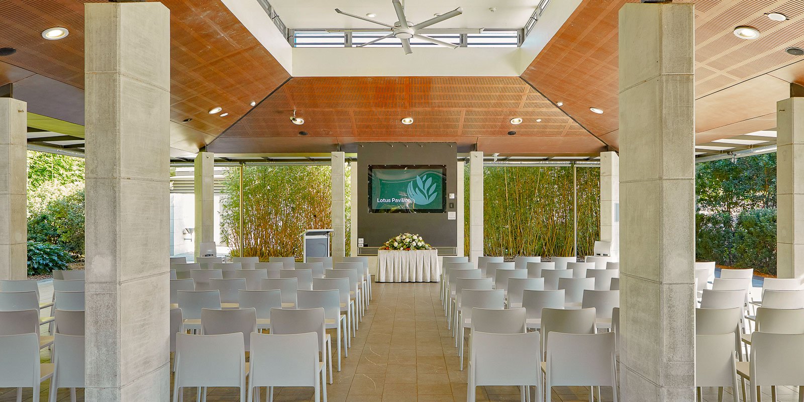 Interior of the Lotus Pavilion with rows of chairs, open design, and greenery visible through the open-air pavilion