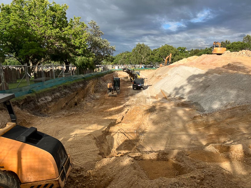 Wide view of excavation work at Pioneer Park with heavy machinery and a large trench, trees and cloudy skies in the background