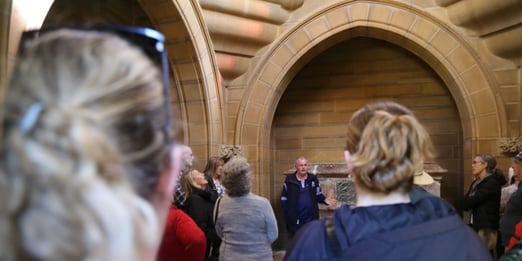 Tour group listening to a guide inside a historic sandstone Frazer mausoleum at Rookwood Cemetery