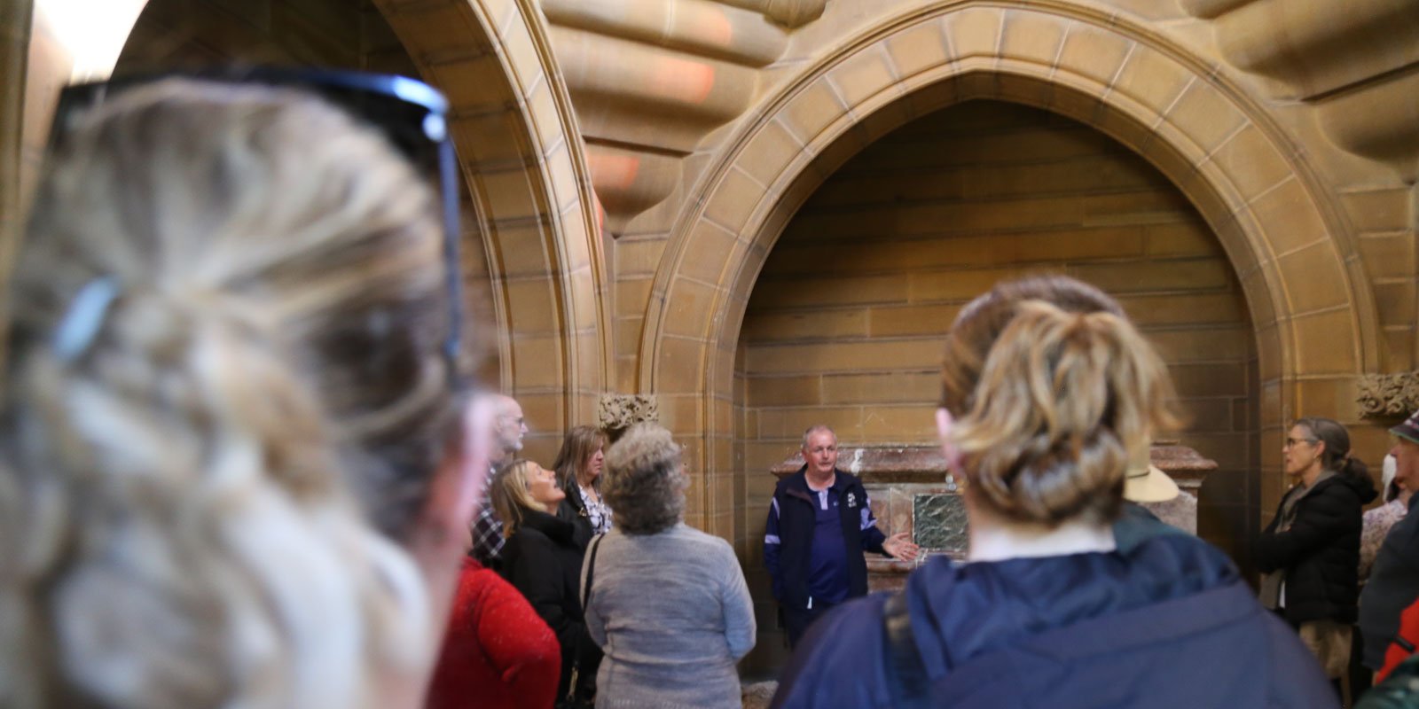 Tour group listening to a guide inside a historic sandstone Frazer mausoleum at Rookwood Cemetery