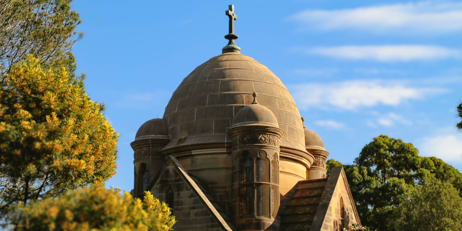 Historic Frazer mausoleum with a domed roof and cross, surrounded by trees under a blue sky