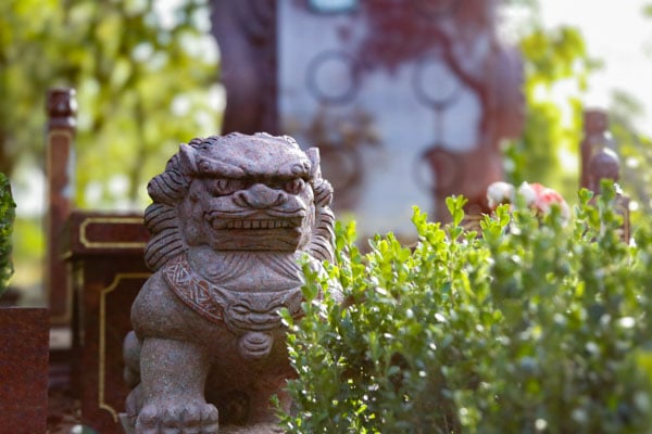 Stone lion statue surrounded by green bushes in a garden at Rookwood Crematorium. The setting is peaceful with sunlight filtering through the trees.