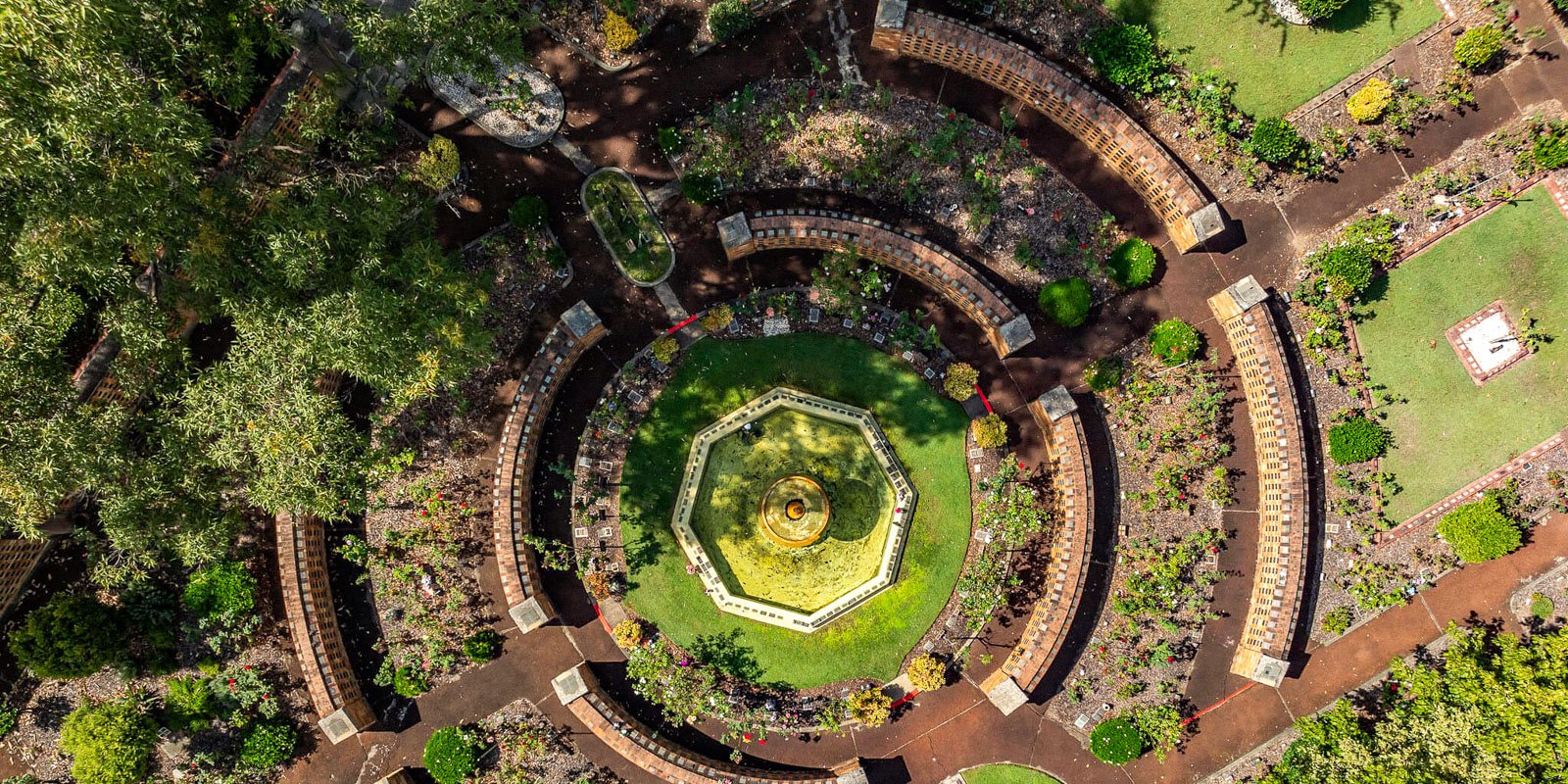 Aerial view of a circular garden with an ornate fountain in the centre. Surrounding the fountain are concentric paths and lush greenery at Rookwood Crematorium.