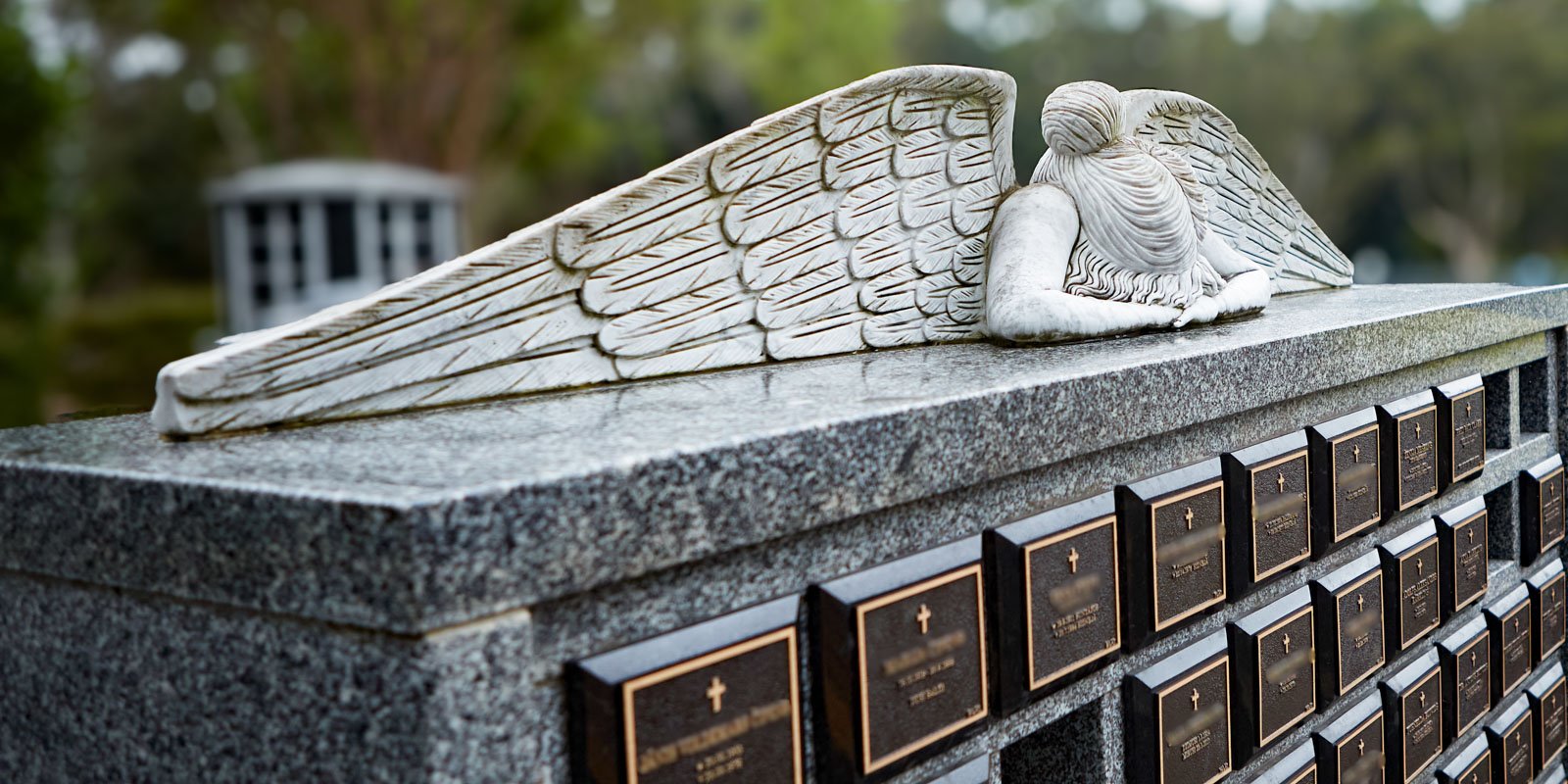 An angel statue lying atop a granite niche wall adorned with memorial plaques at Rookwood General Cemetery and Crematorium.