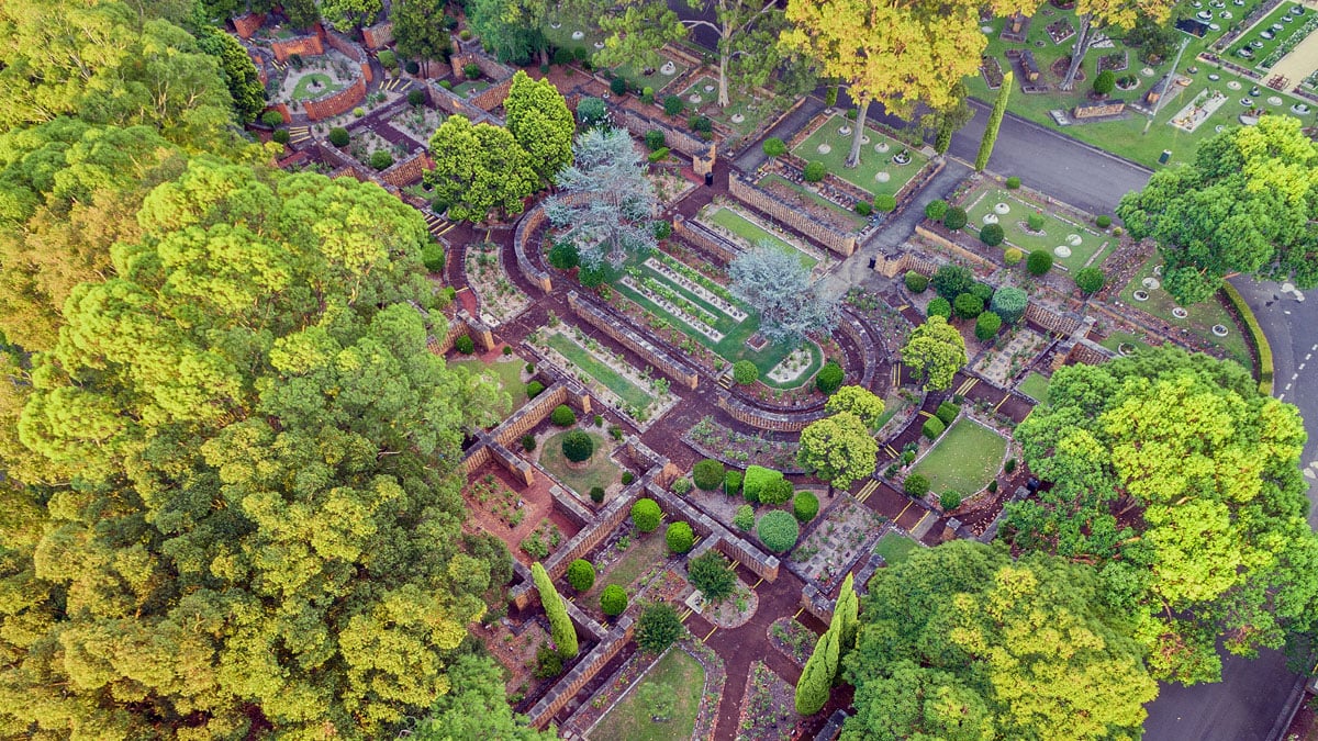 Symmetrical garden with vibrant green trees, winding pathways, and neatly arranged shrubs at Rookwood Crematorium.