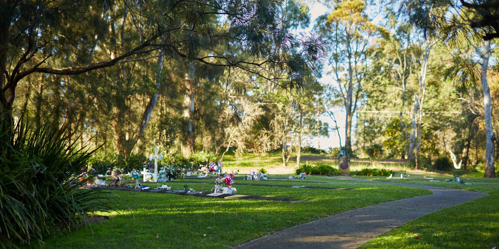 Serene baby lawn area with memorials and flowers surrounded by trees at a peaceful cemetery.