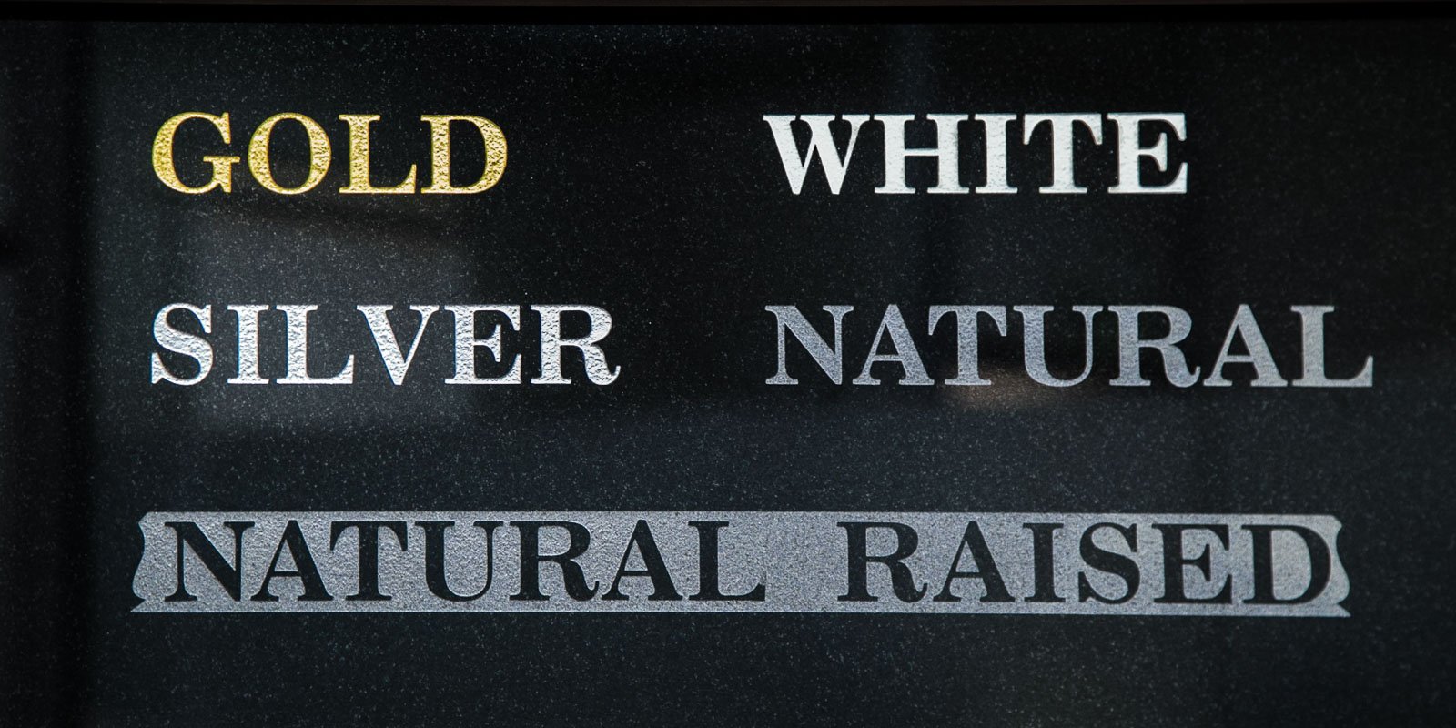 Various inscription styles displayed on a dark stone surface, featuring options in gold, silver, white, and natural raised lettering