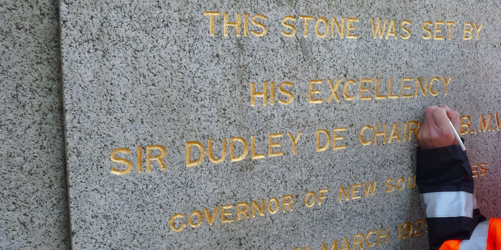 Close-up of a worker restoring gold lettering on a heritage monument inscription, maintaining historical accuracy and craftsmanship.