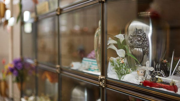 Glass-fronted columbarium niches with memorial urns and personal tributes, including flowers, figurines and keepsakes.