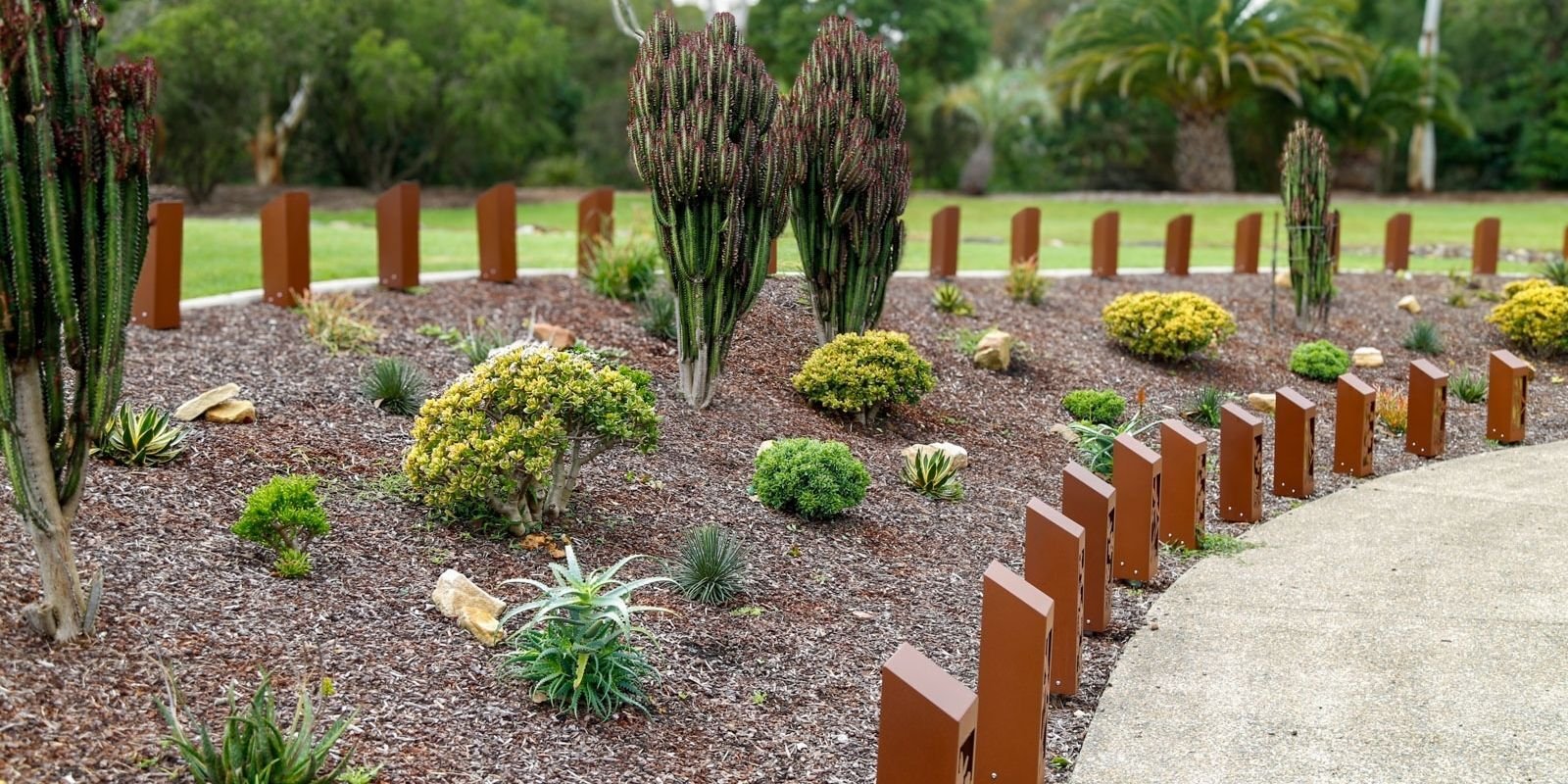 lush natural garden with cactus and shrubs surrounded by mulch. The garden displays steel ash memorialisation totems with bronze plaques.