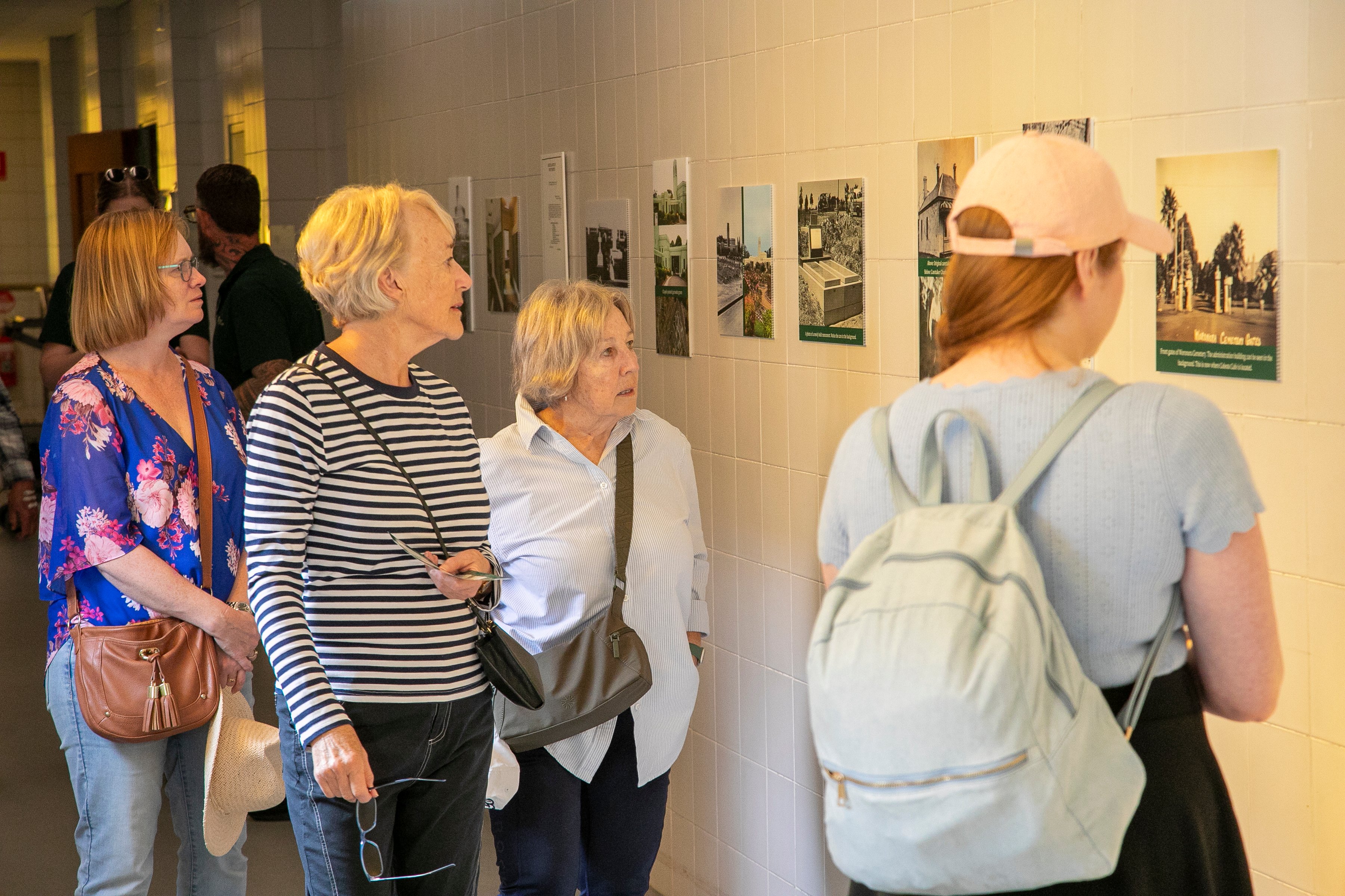A group of four people observes a series of framed photos on a wall in a well-lit hallway. They appear engaged and thoughtful, suggesting an exhibition.